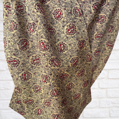 Patterned cravat  with red and gold design on a white brick wall background