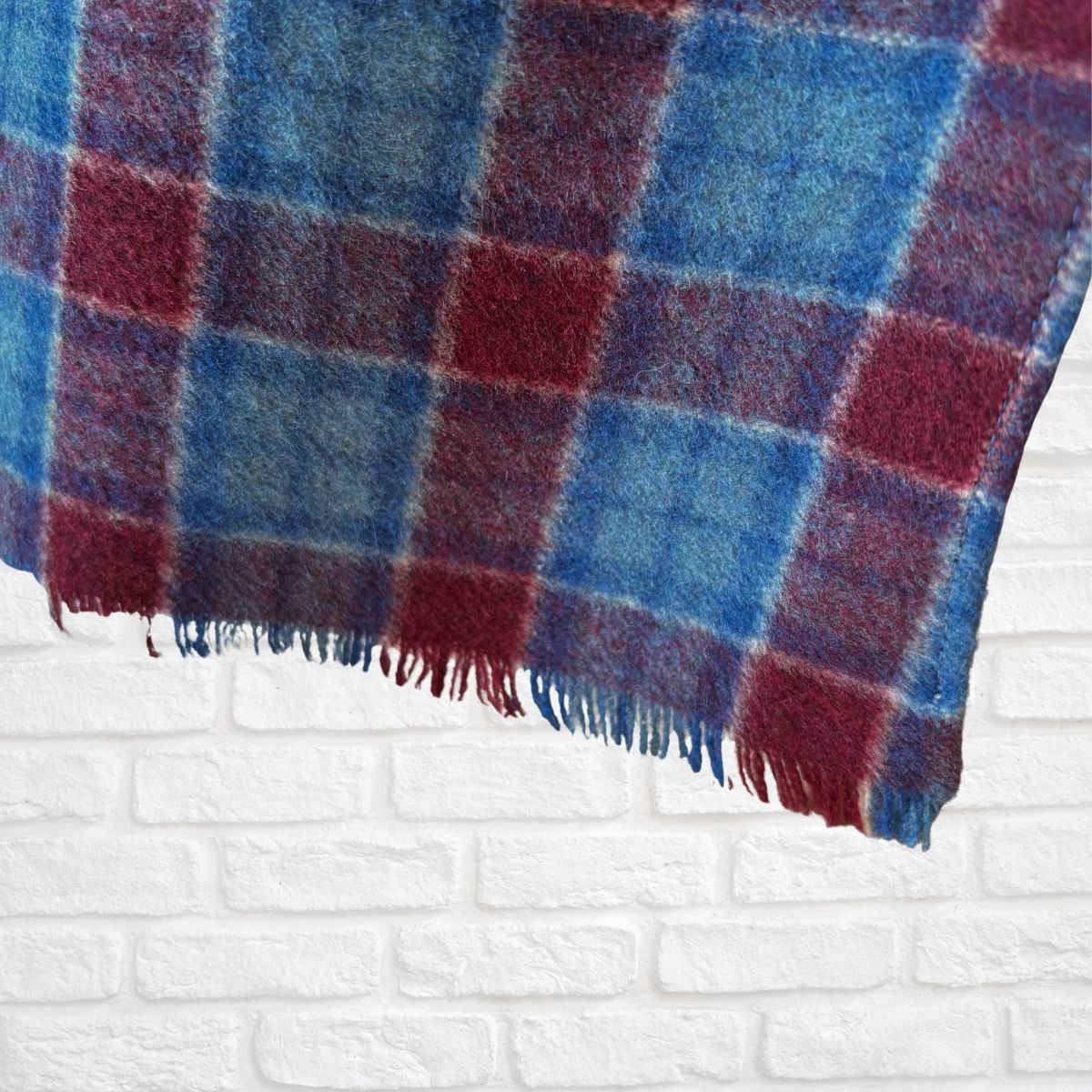 Plaid scarf  with red and blue pattern draped over a white brick wall