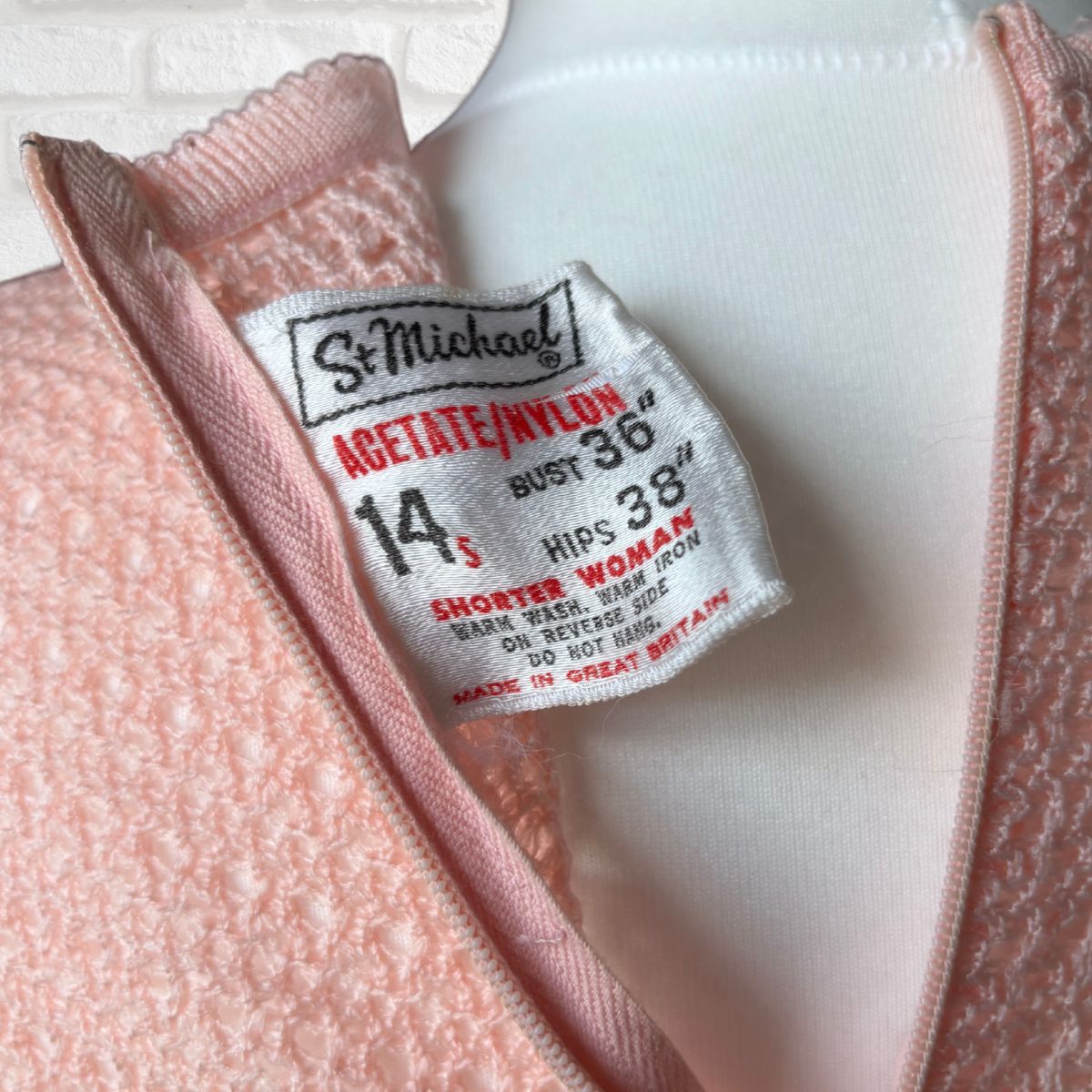 Close-up of a pink textured knit garment with a white inner lining and a visible St. Michael brand size tag reading 14.3.