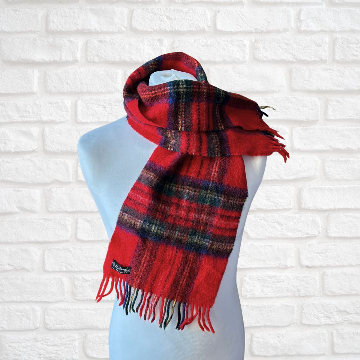 Red plaid scarf on a mannequin against a white brick wall background