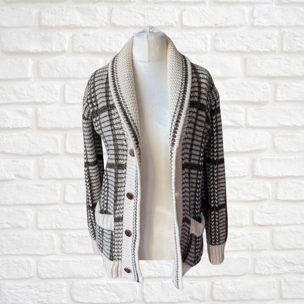 A brown and cream knit cardigan sweater displayed on a white mannequin torso against a white brick wall background.