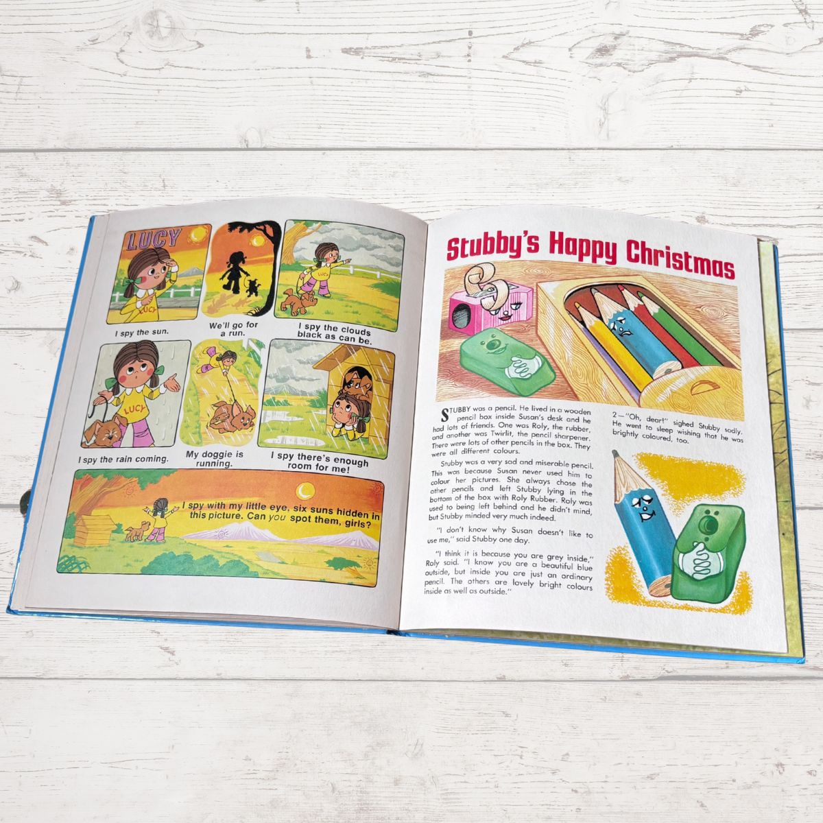 An open children's picture book spread on a white wood surface, showing illustrated pages with the title 'Stubby's Happy Christmas' and colorful cartoon drawings.