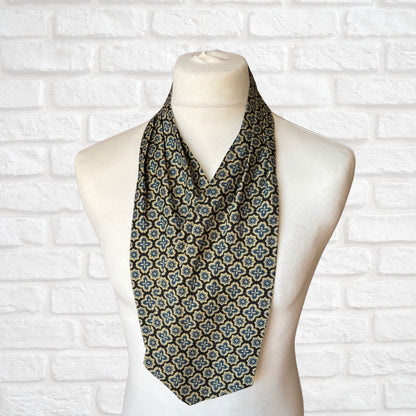 A vintage Austin Reed cravat featuring a black necktie with a cream, gold, and blue stylized floral print, displayed on a mannequin against a white brick wall background.