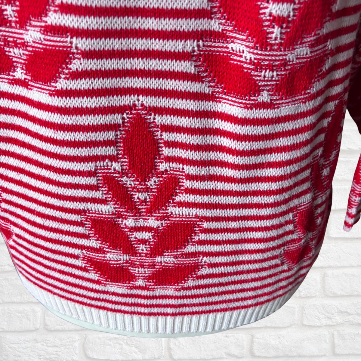 A close-up of a red and white knit sweater featuring horizontal stripes and a large red maple leaf motif knitted into the fabric.