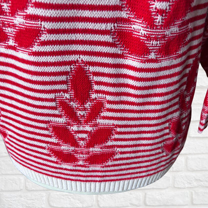 A close-up of a red and white knit sweater featuring horizontal stripes and a large red maple leaf motif knitted into the fabric.