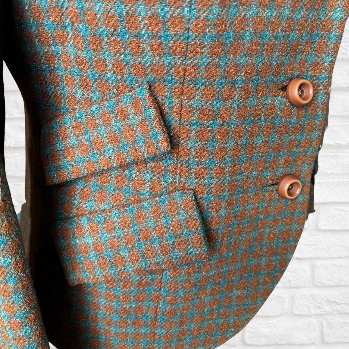 Close-up of a jacket with brown and blue checkered pattern on a white brick wall background