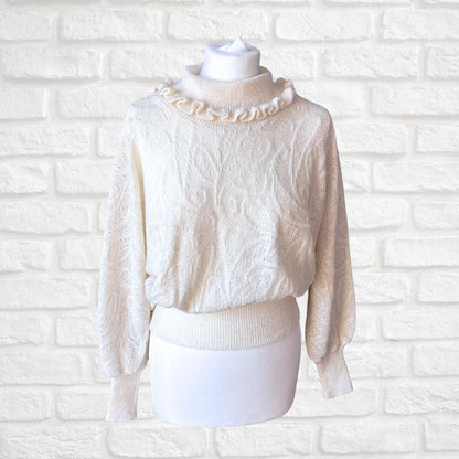 An off-white textured knit sweater with a ruffled mock neck, displayed on a white mannequin torso against a white brick wall background.