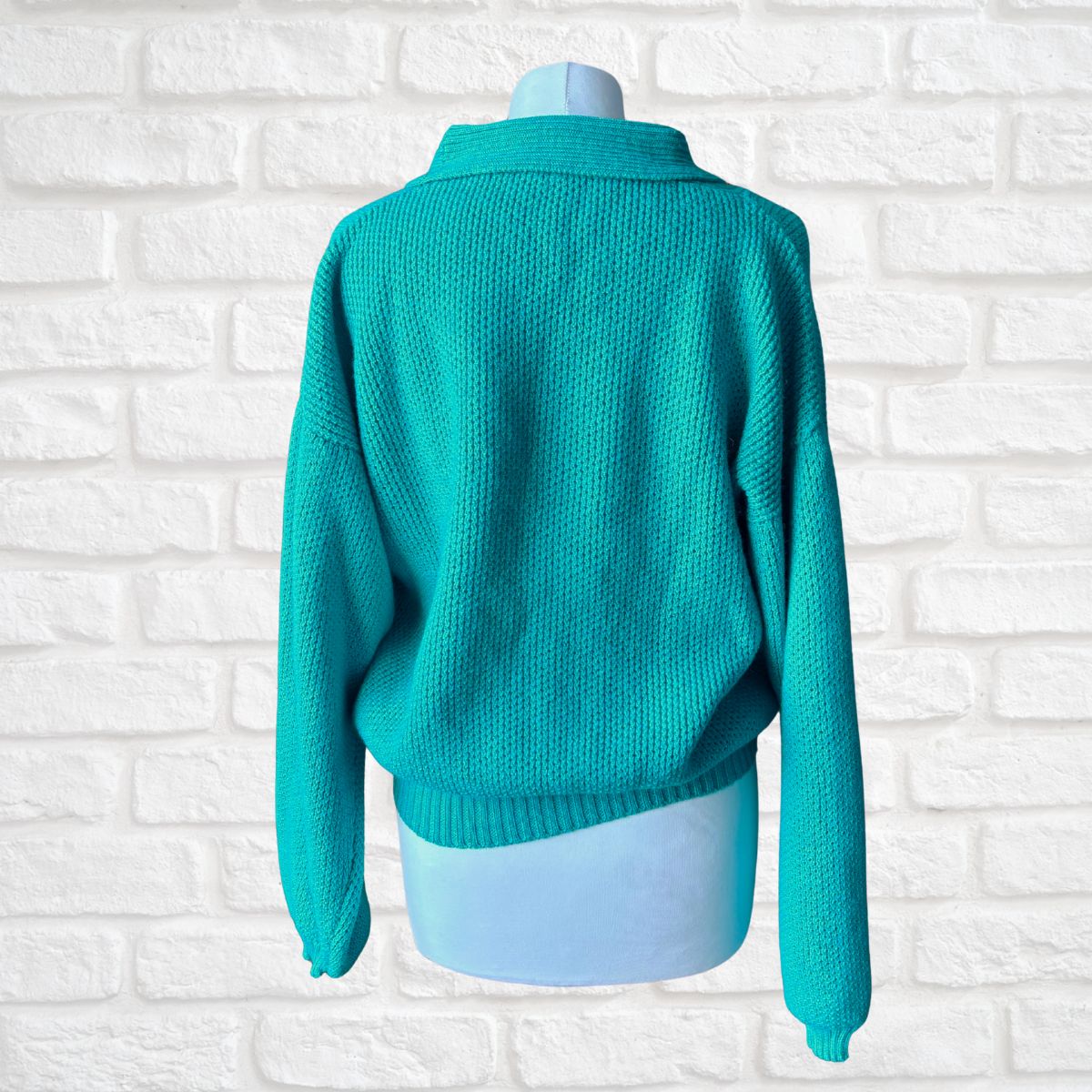 A turquoise knit sweater displayed on a light blue mannequin torso, shown from the back against a white brick wall background.