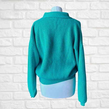 A turquoise knit sweater displayed on a light blue mannequin torso, shown from the back against a white brick wall background.