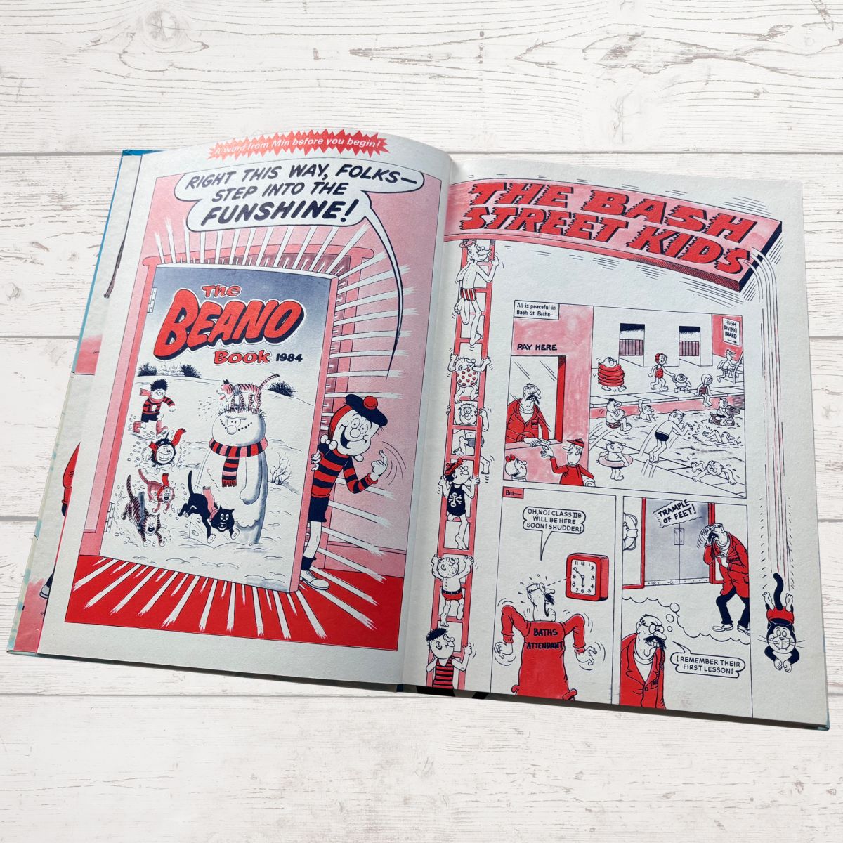 An open vintage comic book or art book laid flat on a white wood surface, showing two spread pages with red, black, and white illustrations and text including 'The Beano Book 1964' and 'The Bash Street Kids.'.