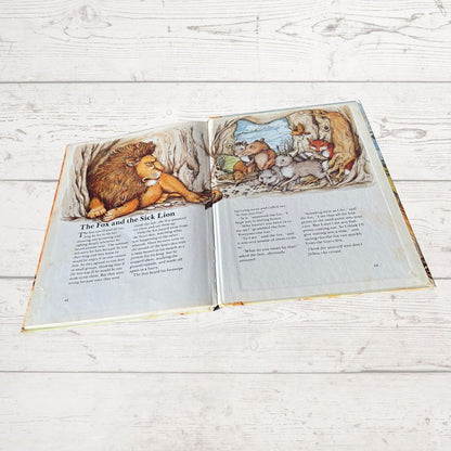 Open book showing illustrations of a lion and fox on a wooden surface