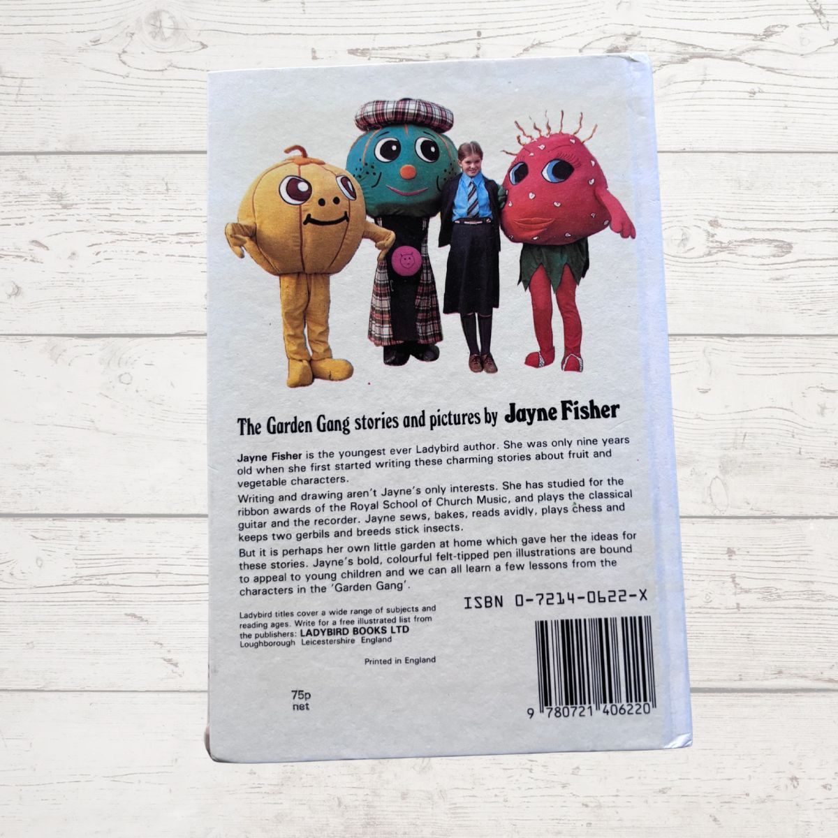 Back cover of a book featuring colorful characters and Jayne Fisher's name on a light wooden surface.