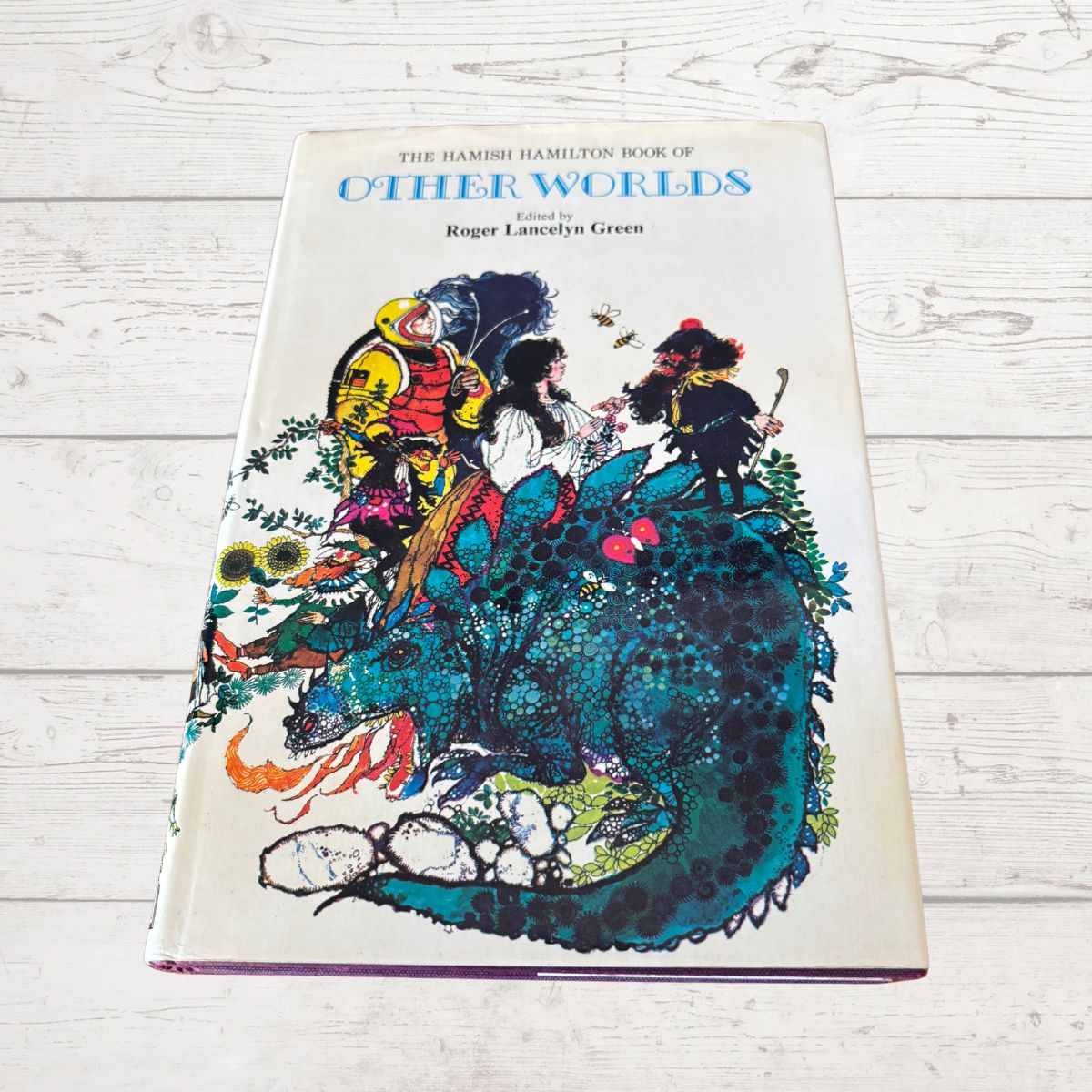 The Hamish Hamilton Book of Other Worlds, a hardcover book with a cream-colored cover and a colorful fantasy illustration, photographed on a white wooden surface.