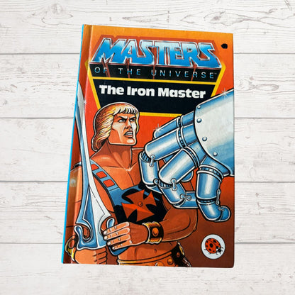 Book cover of 'Masters of the Universe: The Iron Master' on a wooden surface