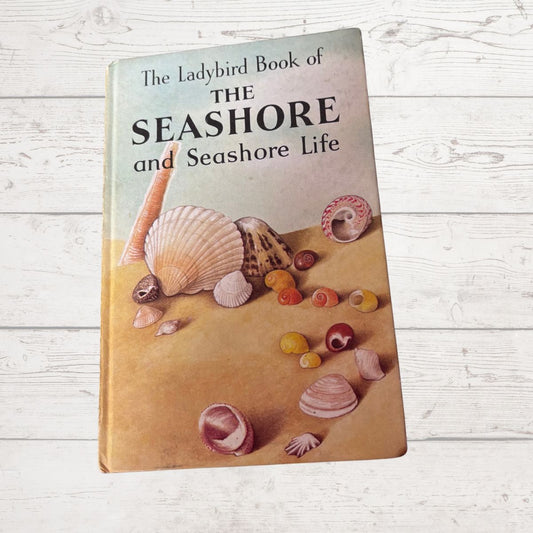 Book titled 'The Ladybird Book of The Seashore and Seashore Life' with illustrations of shells on a wooden surface.