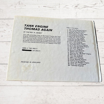 Back cover of a book titled 'Tank Engine Thomas Again' with text and ISBN information on a light wooden surface.