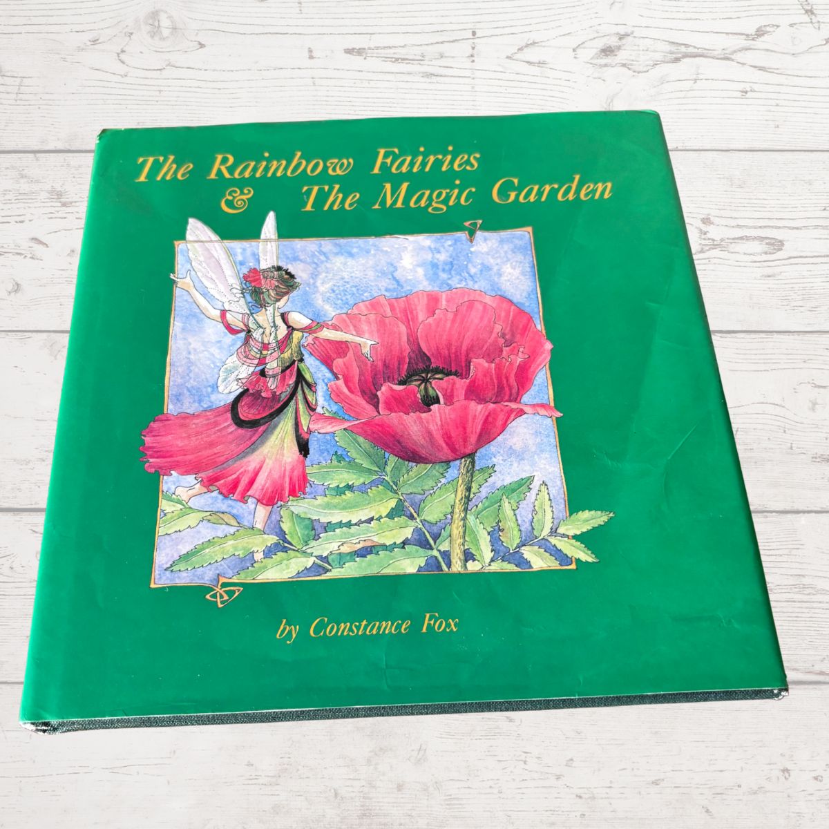 Book titled 'The Rainbow Fairies & The Magic Garden' by Constance Fox on a wooden surface