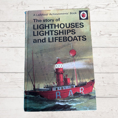 Vintage hardcover book titled 'The story of Lighthouses Lightships and Lifeboats' by Ladybird Achievements, featuring a red lifeboat illustration on the cover, placed on a light wood background.