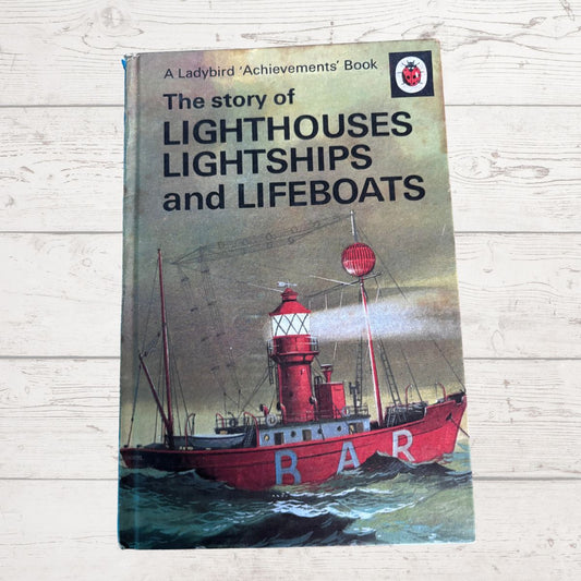 Vintage hardcover book titled 'The story of Lighthouses Lightships and Lifeboats' by Ladybird Achievements, featuring a red lifeboat illustration on the cover, placed on a light wood background.