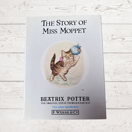 Book cover of 'The Story of Miss Moppet' by Beatrix Potter on a wooden surface