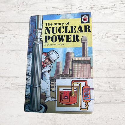 Vintage hardcover book titled 'The story of NUCLEAR POWER' by Ladybird Books, featuring a colorful illustration of a nuclear power plant and worker on a light wood plank background.