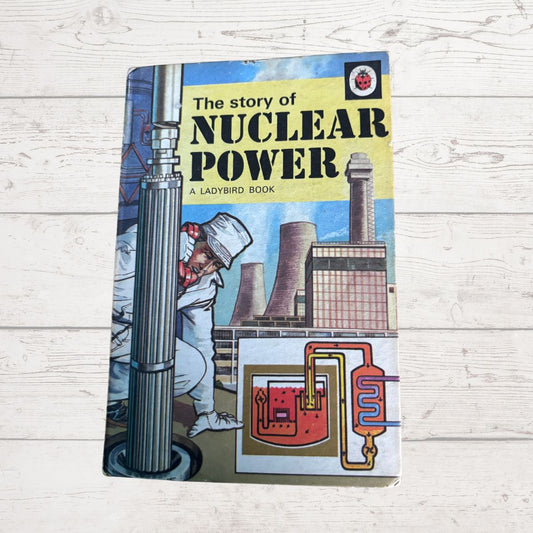 Vintage hardcover book titled 'The story of NUCLEAR POWER' by Ladybird Books, featuring a colorful illustration of a nuclear power plant and worker on a light wood plank background.