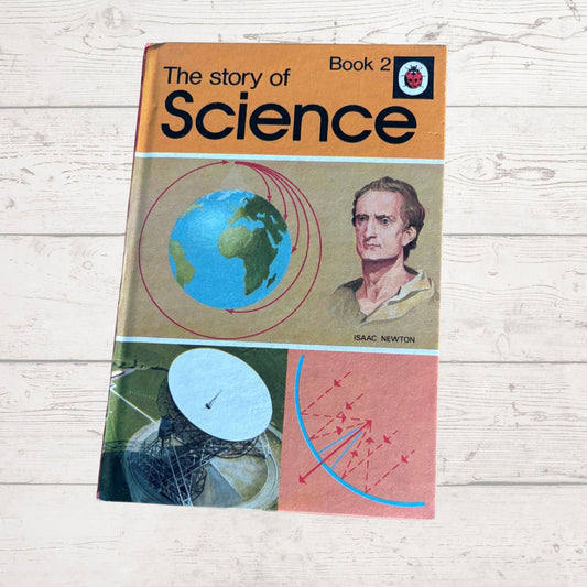 A vintage paperback book titled 'The story of Science Book 2' by Isaac Newton, featuring a colorful cover with illustrations of a globe, a satellite dish, and scientific diagrams, placed on a light wood background.