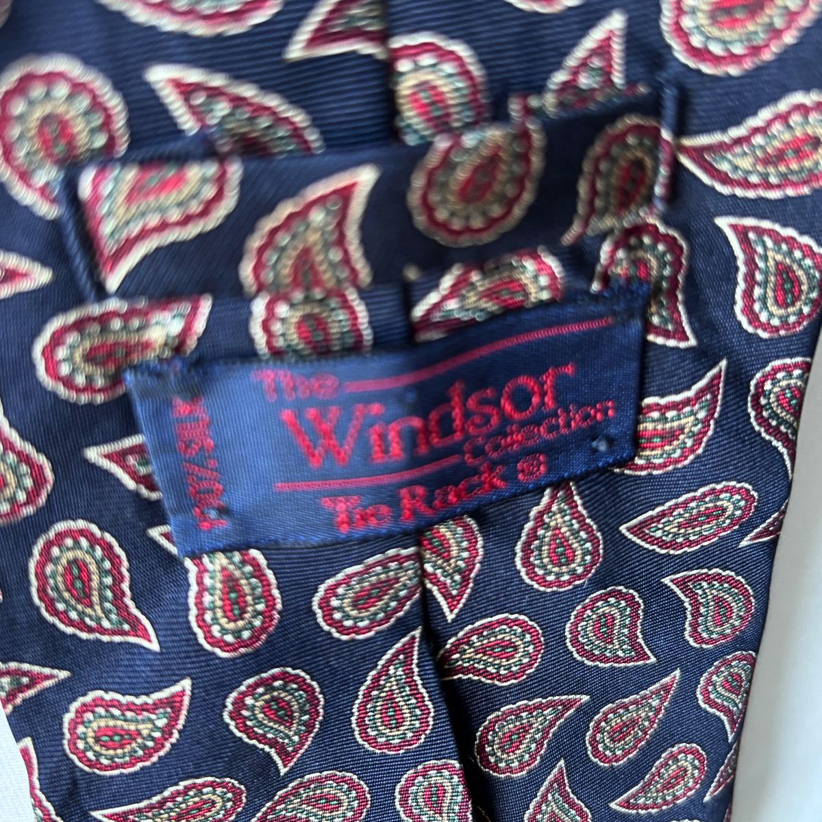 Navy and Red Paisley Silk Vintage Tie On a white brick background - close up of label 