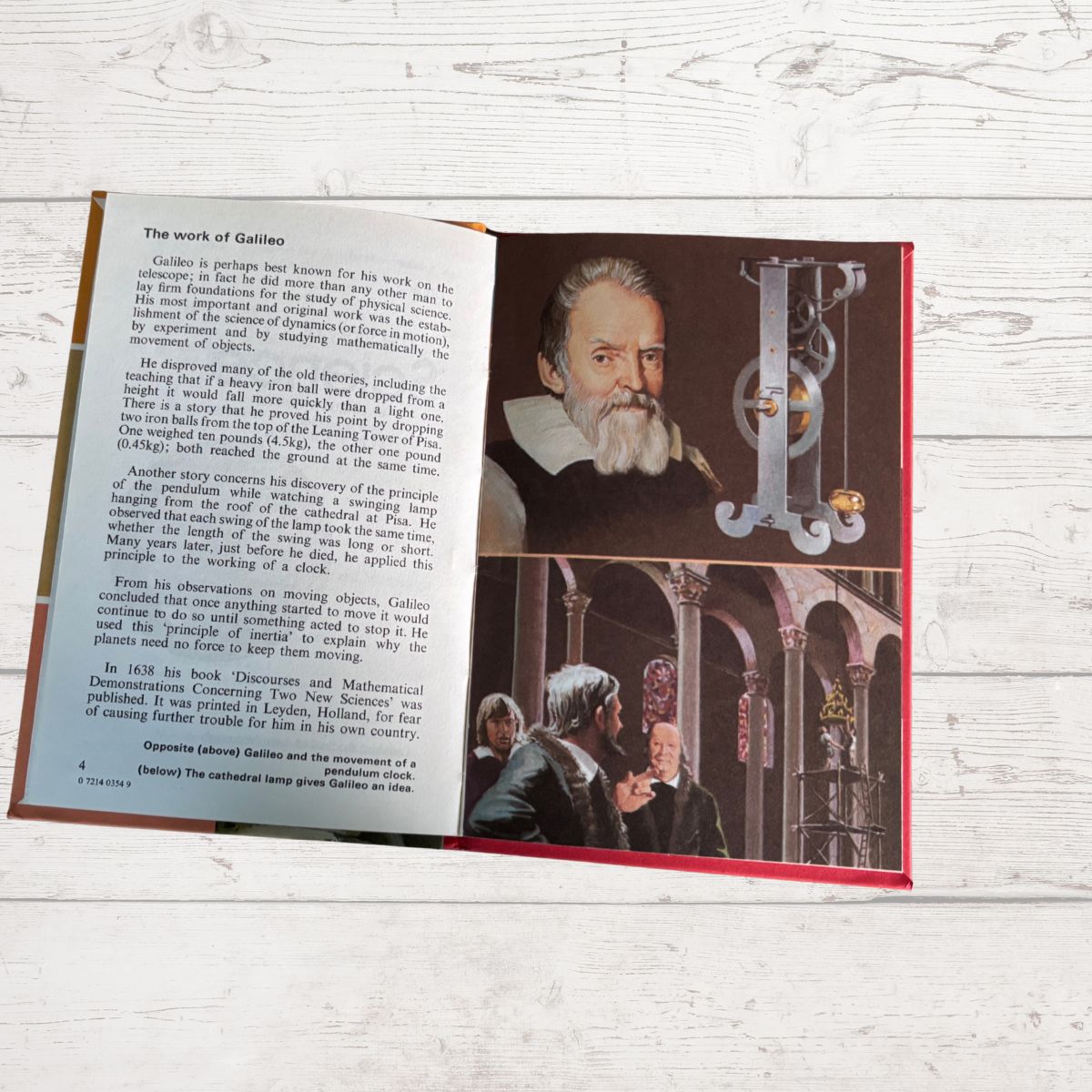 An open book or booklet laid flat on a light wood surface, showing printed text on the left page and a historical photo of Galileo Galilei on the right page, with a red cover edge visible.
