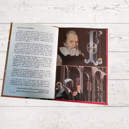 An open book or booklet laid flat on a light wood surface, showing printed text on the left page and a historical photo of Galileo Galilei on the right page, with a red cover edge visible.