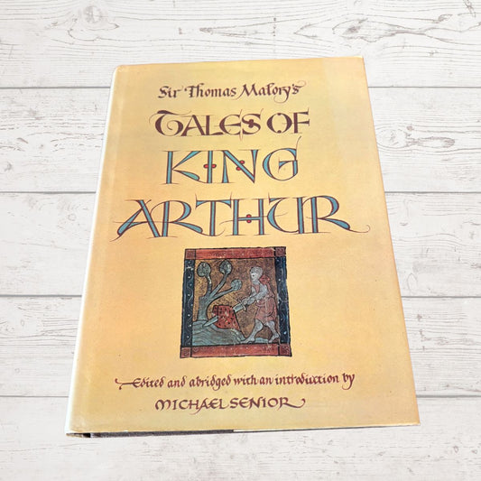 Book titled 'Tales of King Arthur' by Sir Thomas Malory on a wooden surface