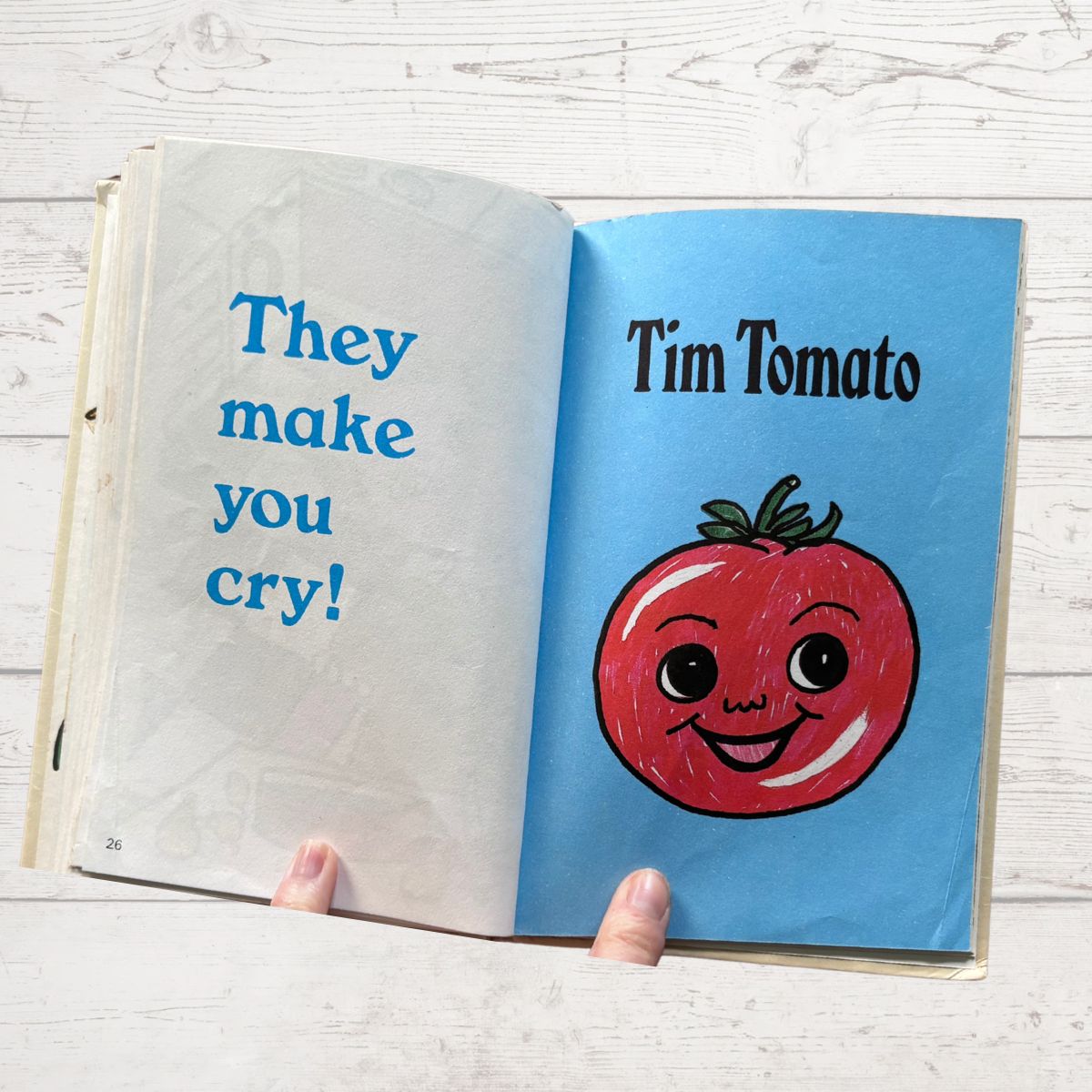 Open book with a cartoon tomato character and text on a wooden surface