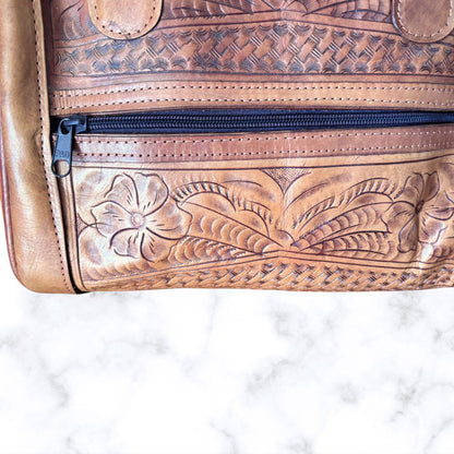 Brown leather bag with intricate patterns and a zipper on a white marble background