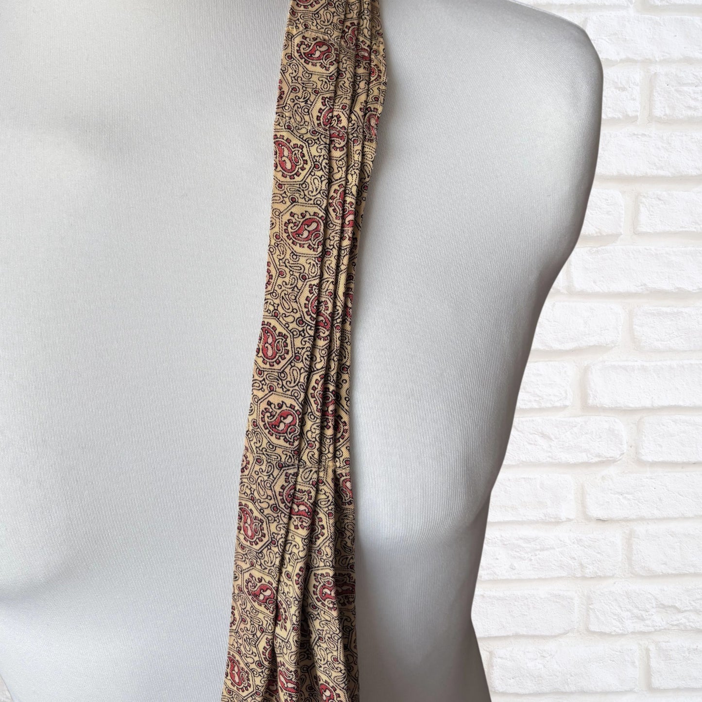 Patterned cravat draped over a mannequin against a white brick wall.