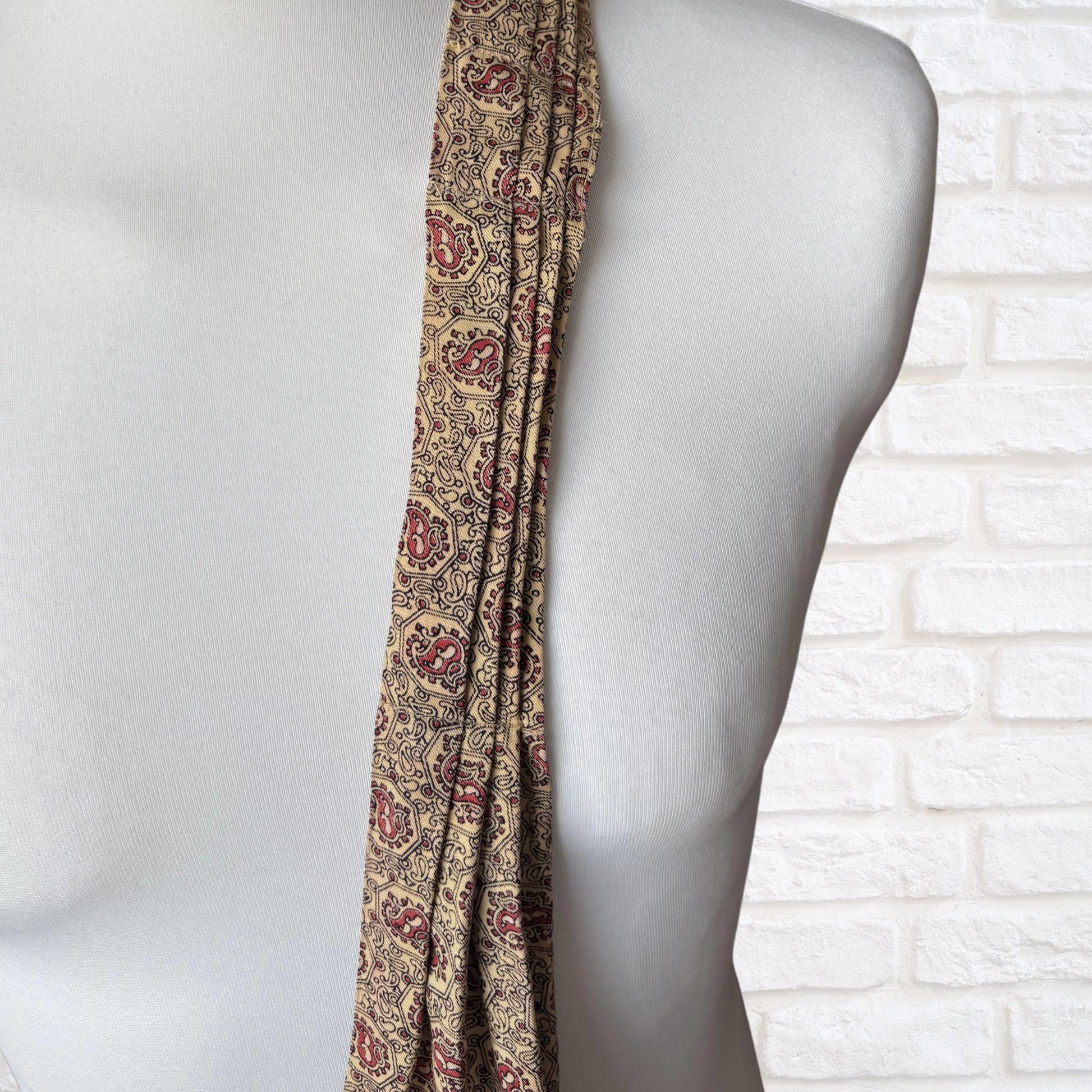 Patterned cravat draped over a mannequin against a white brick wall.