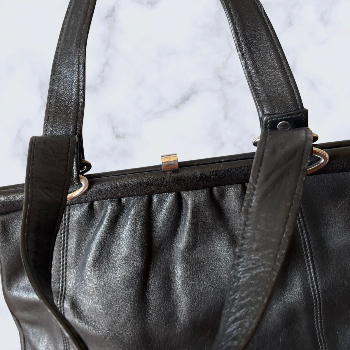 Close-up of a black leather handbag with gold clasp on a light gray background