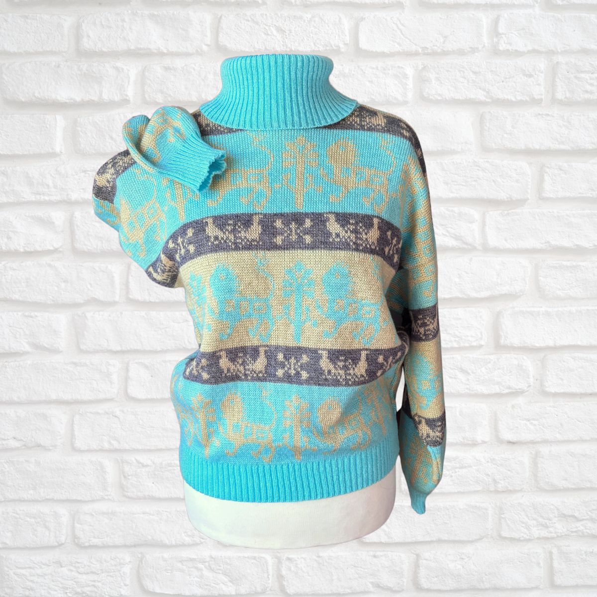 A turquoise and beige knit sweater with a turtleneck, displayed on a white mannequin torso against a white brick wall background.