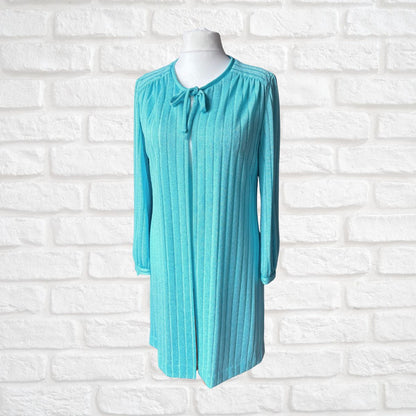 A turquoise blue ribbed knit long-sleeve cardigan with a tie-neck detail, displayed on a white mannequin torso against a white brick wall background.
