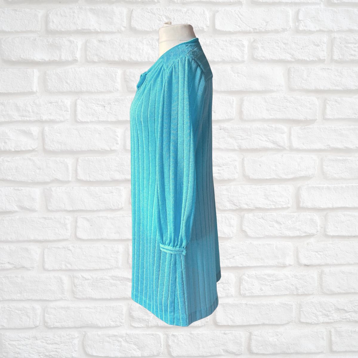 A turquoise blue ribbed long -sleeve cardigan displayed on a mannequin torso against a white brick wall background.