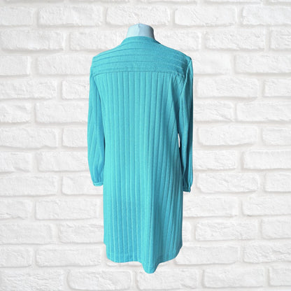 A turquoise ribbed knit long-sleeve cardigan or tunic dress displayed on a mannequin torso against a white brick wall background.