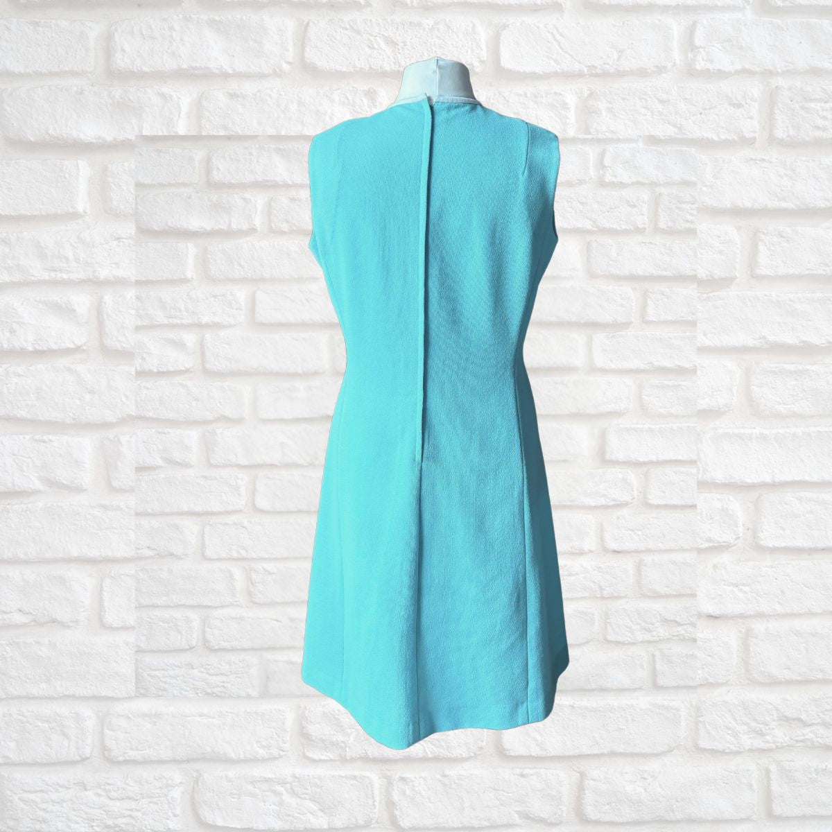 Turquoise dress on a mannequin against a white brick wall background