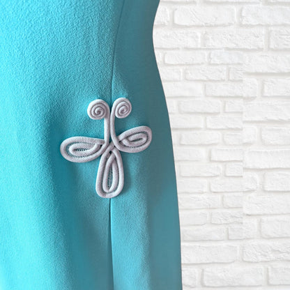 Turquoise dress with decorative white embellishment on a white brick wall background