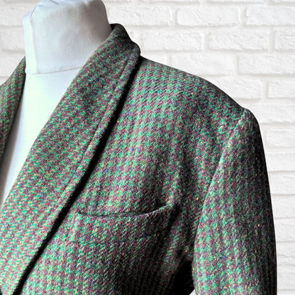 A close-up of a Womens  tweed blazer on a white mannequin torso, featuring a green and brown houndstooth pattern against a white brick wall background.