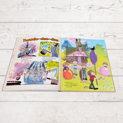 An open children's book spread laid flat on a white wood surface. The left page has colorful comic-style illustrations and text, and the right page shows a whimsical illustrated scene with children, balloons, a house, and a large purple pole.