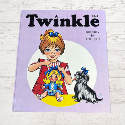 A vintage 1974 children's book titled 'Twinkle' with a lavender cover, featuring an illustration of a girl with blonde hair in a red dress and a small black-and-white dog. The book is photographed on a white wood surface.