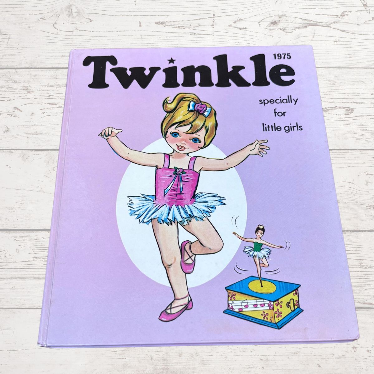 A vintage 1975 children's book titled 'Twinkle' with the subtitle 'specially for little girls,' featuring an illustration of a ballerina on a light purple cover, photographed on a whitewashed wood surface.