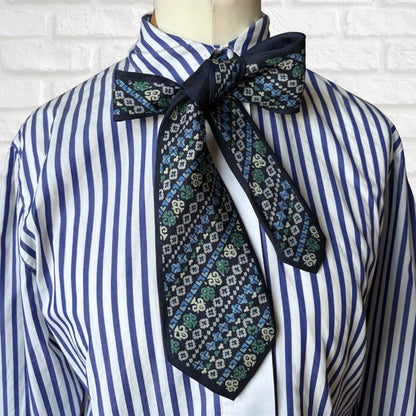 Blue and white striped shirt with a patterned tie on a mannequin against a white brick wall.