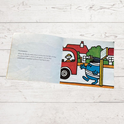 Open book with a colorful illustration of a character Mr Bump near a bus stop on a wooden surface