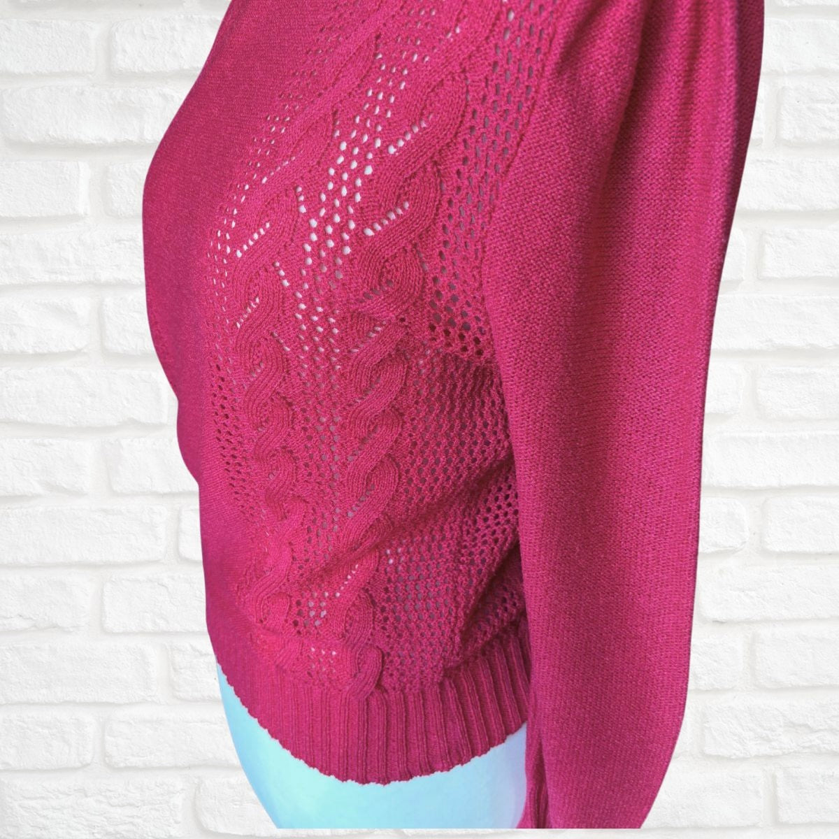 Close-up of a pink knitted sweater against a white brick wall.