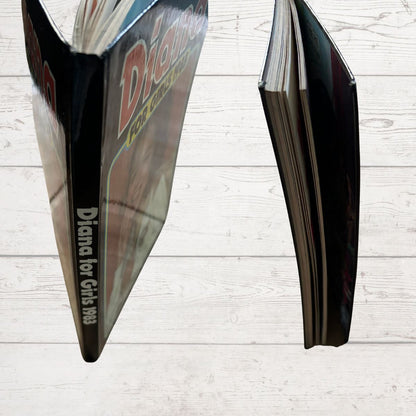 Open book showing the spine and corners with 'Diana' branding on a light wooden surface